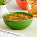 A close-up of an Acopa Capri palm green stoneware bistro bowl filled with soup and herbs.