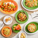 An Acopa Valencia orange oval coupe platter on a table with a bowl of noodles and vegetables and plates of food.