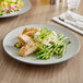 A matte grey and black Acopa Apollo coupe melamine plate with chicken and green beans on a table.