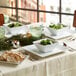 A table with Acopa white square plates of food and a bowl of salad.