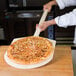 A person using an American Metalcraft wood pizza peel to take a pizza out of the oven.