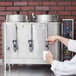 A person pouring coffee into a Cecilware automatic coffee urn.
