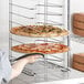 A person holding a pizza on a Choice aluminum wide rim pizza pan rack.