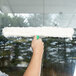 A person cleaning a window with a Unger white plastic T-bar.