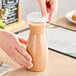 A person pouring chocolate milk into a Cambro plastic beverage decanter.