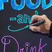 A hand using a black Wet Erase marker to write on a blackboard.