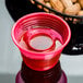 A red Fineline plastic cup with liquid next to peanuts.