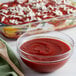 A wooden spoon in a bowl of Bella Vista crushed tomatoes next to a casserole dish.