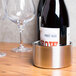 A bottle of wine in a stainless steel wine coaster on a table next to two wine glasses.