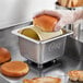 A person using a Choice stainless steel butter spreader to cut a brown bun.