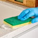 A gloved hand using a yellow sponge.
