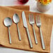 A Acopa Petra stainless steel flatware set on a napkin with yellow roses on a table.