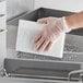 A hand in a plastic glove cleaning a stove with a Lavex Super Soft White Scouring Pad.