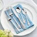 A white plate with Acopa Ophelia stainless steel flatware on a blue surface.