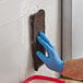 A person wearing a blue glove using a Lavex brown multi-purpose scouring pad to clean a wall.