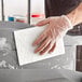 A person wearing a glove cleaning a surface with a Lavex white scouring pad.