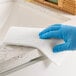 A hand in a blue glove using a Lavex white scouring pad to clean a countertop.
