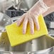 A person in gloves cleaning a pot with a Lavex yellow cellulose sponge.