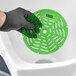 A person in black gloves using a green Lavex melon scented urinal screen in a toilet.