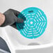 A hand in a black glove holding a blue Lavex Ocean Breeze Scent Deodorized Gel Urinal Screen with holes in it.