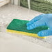 A gloved hand using a Lavex yellow cellulose sponge to clean a counter.