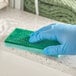 A gloved hand using a Lavex green sponge to clean a counter.