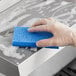 A hand in a glove using a Lavex blue sponge to clean a stainless steel sink.