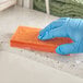 A hand in a blue glove cleaning a counter with an orange sponge.