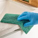 A gloved hand using a Lavex green scouring pad to clean a counter.