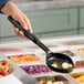 A hand holding a black Vollrath spoodle over a tray of vegetables.