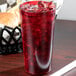 A Cambro ruby red plastic tumbler filled with red liquid and ice on a table with a burger.