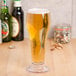 A customizable footed plastic pilsner glass full of beer on a table.