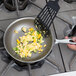 A person cooking scrambled eggs and vegetables in a Vollrath Wear-Ever aluminum non-stick fry pan.