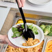 A person holding a plate of salad with a black Carlisle salad bar spoon.
