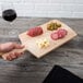 A hand holding an American Metalcraft wood serving peel with food on it over a table set with a glass of red wine.