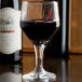 A Libbey wine glass of red wine sits on a table next to a bottle.