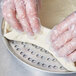 A person in plastic gloves using an American Metalcraft Super Perforated Pizza Pan to make dough.