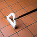 A person using a white Carlisle Sparta Spectrum grout brush to clean a tile floor.