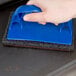 A hand using a blue Winco Grill Screen to clean a grill.