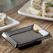 A black rectangular Carlisle ramekin with brown sauce next to a plate of sushi.