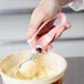 A hand using a Vollrath pink #60 scoop with pink handle to scoop ice cream.