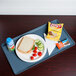 A teal Cambro dietary tray with a sandwich, chips, and a drink on it.