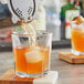 A person pouring orange juice into an Anchor Hocking Clarisse old fashioned glass filled with ice and orange juice.
