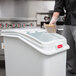 A man in a chef's uniform using a Rubbermaid ingredient bin with a white lid to scoop rice into a container.