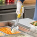 A person in gloves using a Vollrath Jacob's Pride yellow handled spoon to serve white food.