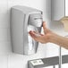 A hand using a gray Health Guard hand soap / sanitizer dispenser.