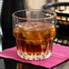 A Libbey Everest stackable rocks glass with a drink of brown liquid and ice on a table.