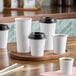 A wooden tray with four white Choice paper cups with black lids.