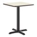 A square standard height table with a reversible white birch or ash laminated top and a black cast iron base.