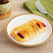 A Bridor cherry Greek yogurt danish on a plate next to a cup of coffee with a fork.